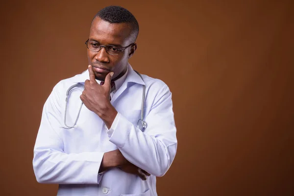 Estúdio tiro de jovem médico homem africano contra fundo marrom — Fotografia de Stock