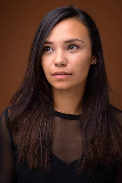 Studio shot van jonge Aziatische vrouw tegen bruine achtergrond — Stockfoto