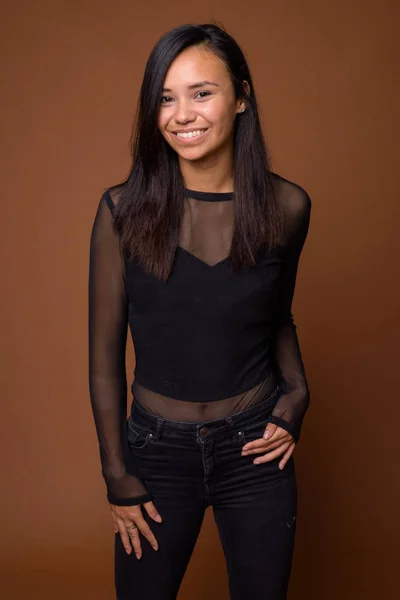 Studio shot of young Asian woman against brown background — Stock Photo, Image