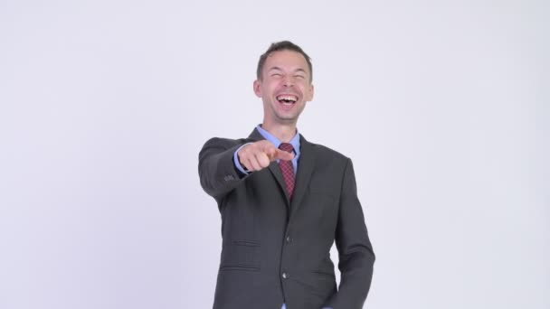 Студийный кадр счастливого бизнесмена, смеющегося и указывающего на камеру — стоковое видео
