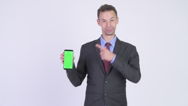 Studio colpo di uomo d'affari felice mostrando telefono e dando pollici in su — Video Stock