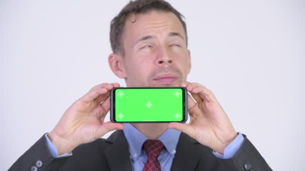 Studioaufnahme eines glücklichen Geschäftsmannes, der beim Vorzeigen seines Telefons denkt — Stockvideo