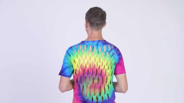 Rear view of man with tie-dye shirt looking back and waving hand — Stock Video