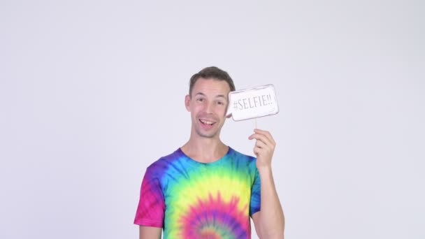 Studio shot van gelukkig man met tie-dye shirt houden selfie papier teken — Stockvideo