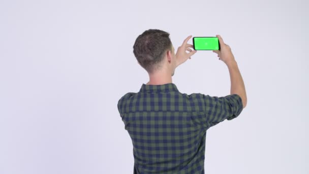 Вид сзади на хипстера, фотографирующегося с телефоном — стоковое видео