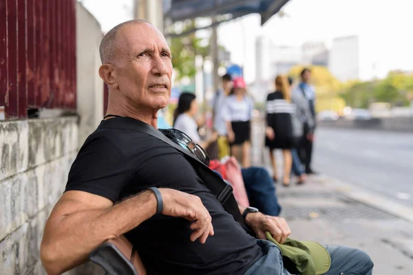 Bald senior tourist man waiting and sitting on wooden bench at t — Stock Photo, Image