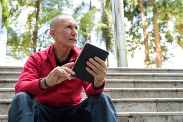 Bald senior man thinking and holding digital tablet while sittin