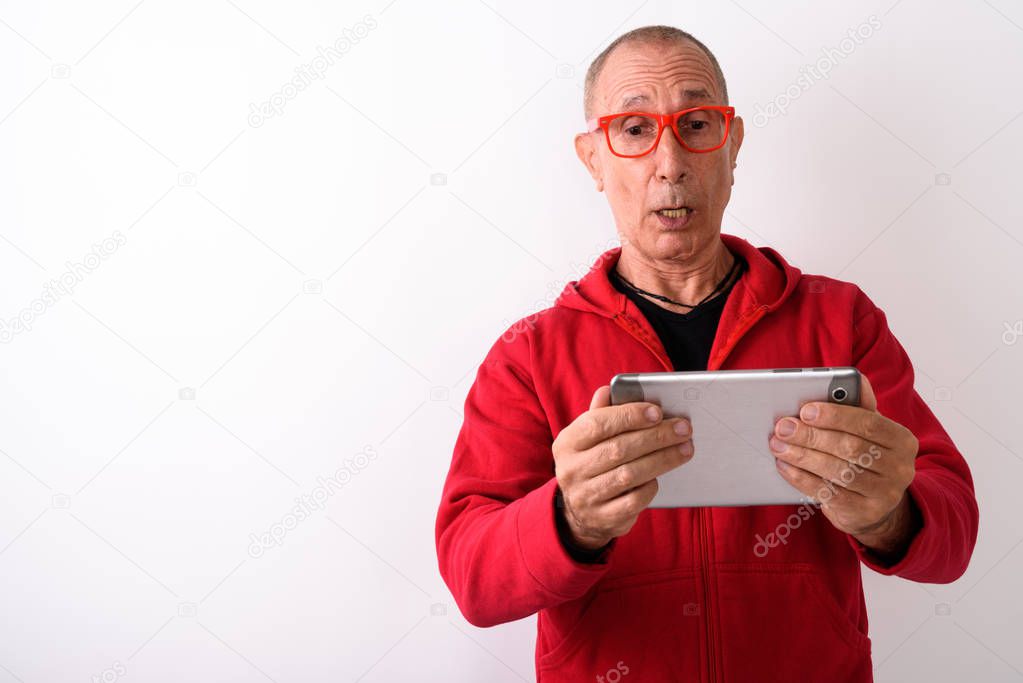 Studio shot of bald senior man using digital tablet while lookin