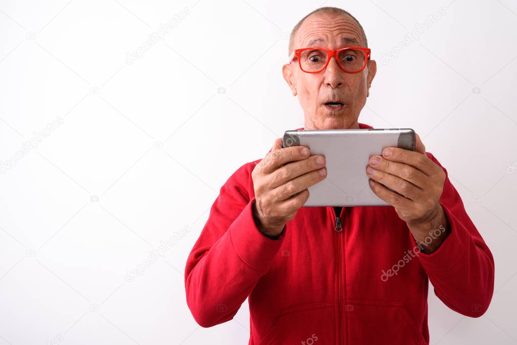 Studio shot of shocked bald senior man using digital tablet whil