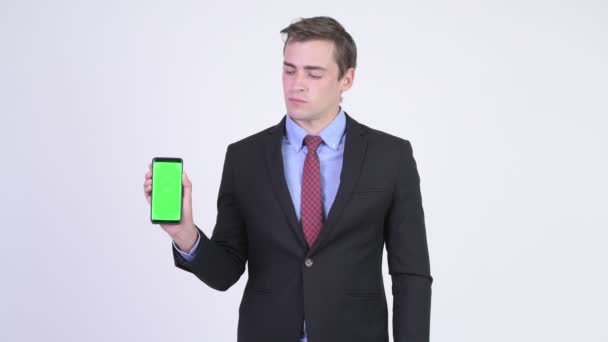 Joven feliz hombre de negocios guapo mostrando el teléfono y dando pulgares hacia arriba — Vídeos de Stock