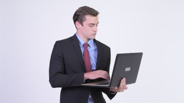 Молодой счастливый красивый бизнесмен думает во время использования ноутбука — стоковое видео