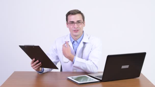 Jovem feliz bonito homem médico explicando algo contra mesa de madeira — Vídeo de Stock