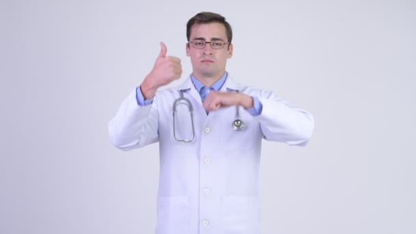 Молодой красивый мужчина врач выбирает между большим и большим пальцами вниз — стоковое видео