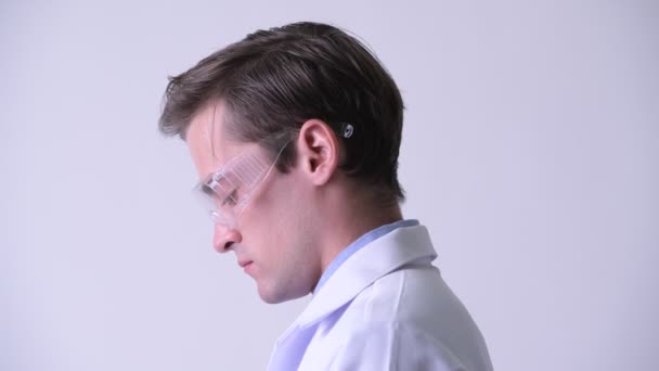 Vista del perfil del joven guapo doctor con gafas protectoras y mirando hacia arriba — Vídeos de Stock