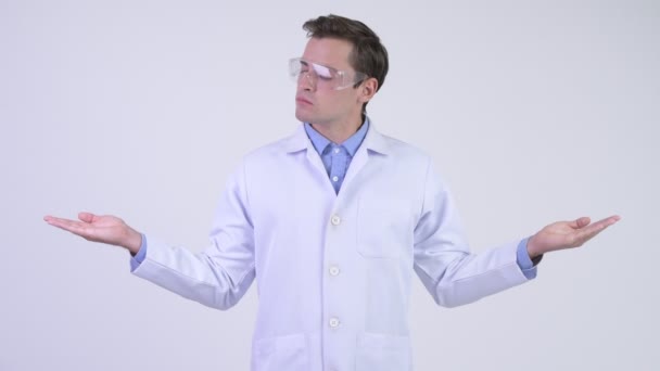 Jovem médico bonito vestindo óculos de proteção e comparando algo — Vídeo de Stock