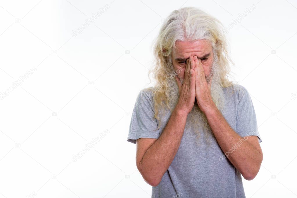 Studio shot of senior bearded man crying while covering face wit