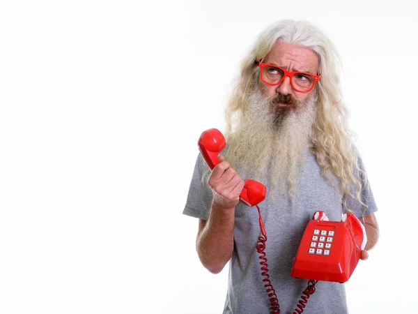 Studio shot of senior bearded man holding old telephone while th — Stock Photo, Image