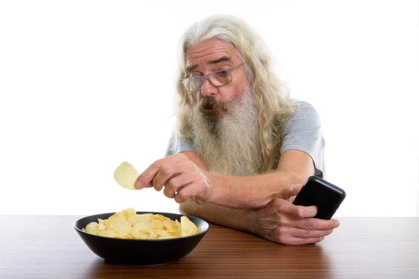 Studio záběr senior vousatý muž drží mobilní telefon eat — Stock fotografie