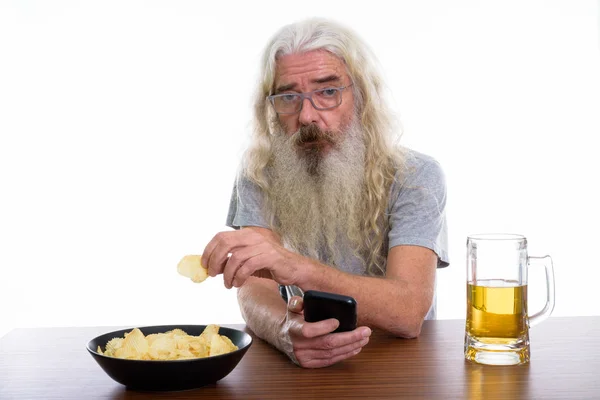 Prise de vue en studio d'un homme barbu tenant un téléphone portable pendant qu'il mange — Photo