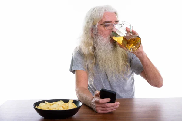 Studio shot of senior bearded man using mobile phone while drink — Stock Photo, Image