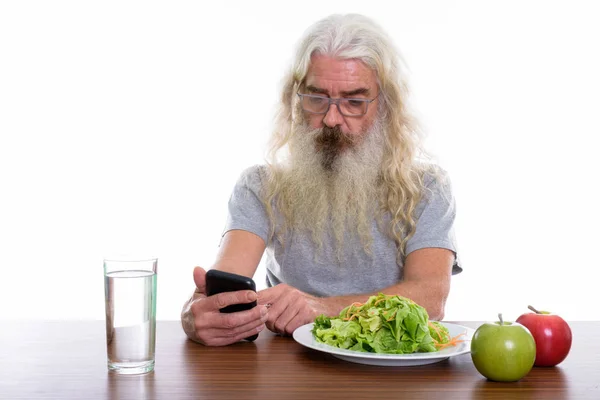 Studio shot van senior bebaarde man met behulp van mobiele telefoon met gezondheid — Stockfoto