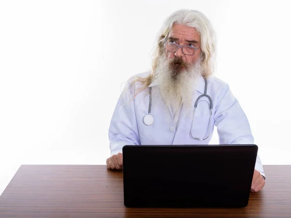 Studio shot of senior bearded man doctor thinking while using la — Stock Photo, Image