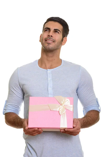 Jovem homem persa feliz sorrindo e segurando caixa de presente enquanto pensa — Fotografia de Stock