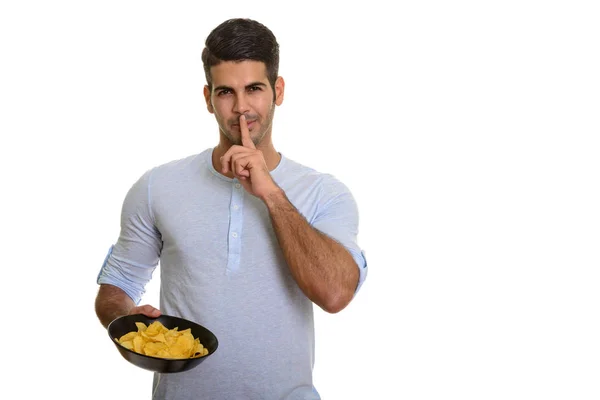 Young handsome Persian man holding bowl of potato chips with fin Royalty Free Stock Photos
