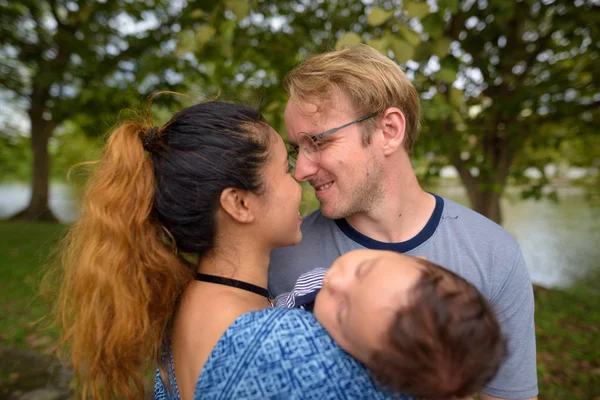 Multiethnische junge Familie, die sich im Park zusammenschließt — Stockfoto