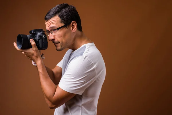 Retrato de homem fotógrafo tirando foto contra fundo marrom — Fotografia de Stock