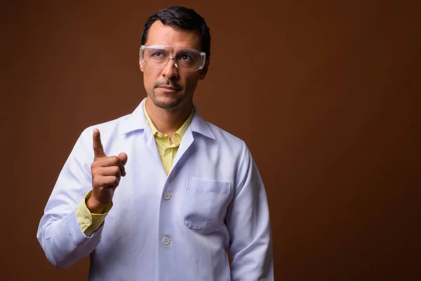 Мужчина-врач в защитных очках, показывая пальцем вверх и думая: — стоковое фото