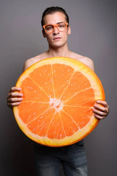 Jovem homem bonito sem camisa segurando grande fatia de fruta laranja — Fotografia de Stock