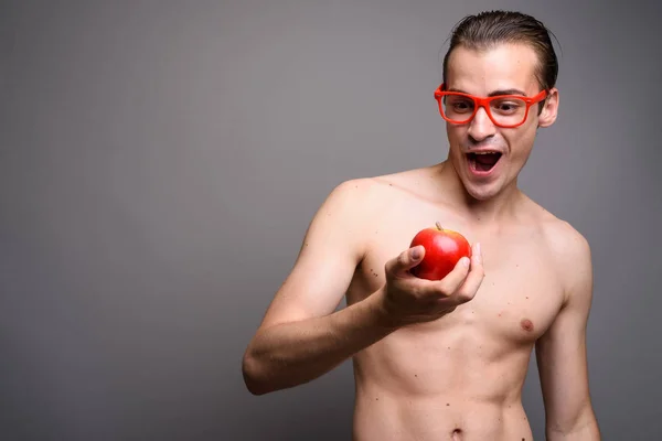 Verbaasd knappe man shirtless bedrijf rode appel tegen een grijze achtergrond — Stockfoto