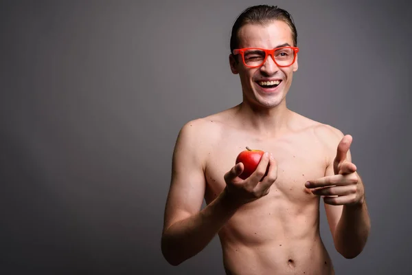 Joven hombre guapo sin camisa sosteniendo manzana roja mientras guiña y señala con el dedo — Foto de Stock