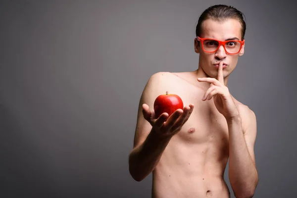 Jovem homem bonito sem camisa segurando maçã vermelha com o dedo nos lábios — Fotografia de Stock