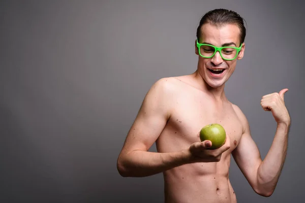 Joven hombre guapo sin camisa sosteniendo manzana sobre fondo gris — Foto de Stock