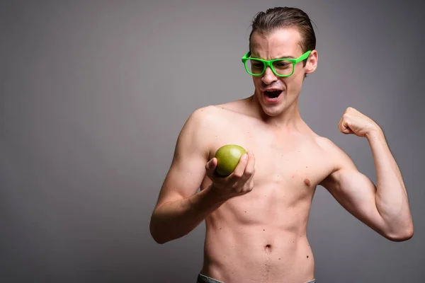 年轻英俊的男子赤裸上身握着苹果, 同时弯曲他的二头肌 — 图库照片