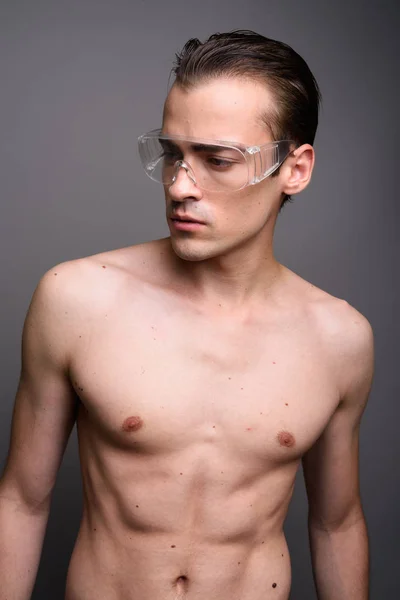 Joven hombre guapo sin camisa usando gafas protectoras contra fondo gris — Foto de Stock