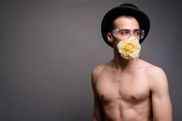 Giovane bell'uomo senza maglietta indossando cappello e avendo fiore in bocca — Foto Stock
