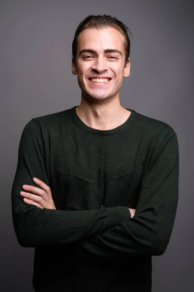 Jovem homem feliz sorrindo com os braços cruzados contra fundo estúdio cinza — Fotografia de Stock