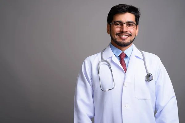 Young handsome bearded Persian man doctor against gray backgroun — Stock Photo, Image