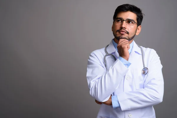 Junger gutaussehender bärtiger persischer Mann Arzt gegen grauen Hintergrund — Stockfoto