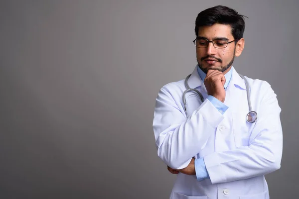 Jovem bonito barbudo persa homem médico contra cinza backgroun — Fotografia de Stock