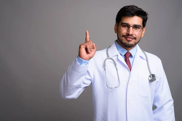 Jovem bonito barbudo persa homem médico contra cinza backgroun — Fotografia de Stock