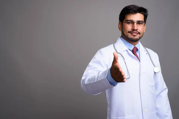 Young handsome bearded Persian man doctor against gray backgroun — Stock Photo, Image