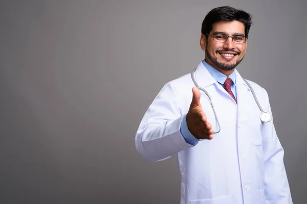 Young handsome bearded Persian man doctor against gray backgroun — Stock Photo, Image