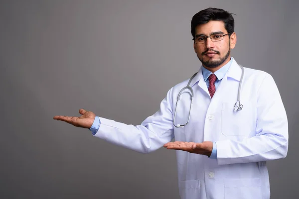 Young handsome bearded Persian man doctor against gray backgroun — Stock Photo, Image