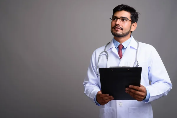 Jovem bonito barbudo persa homem médico contra cinza backgroun — Fotografia de Stock