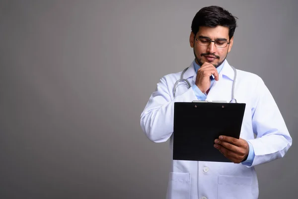 Young handsome bearded Persian man doctor against gray backgroun — Stock Photo, Image