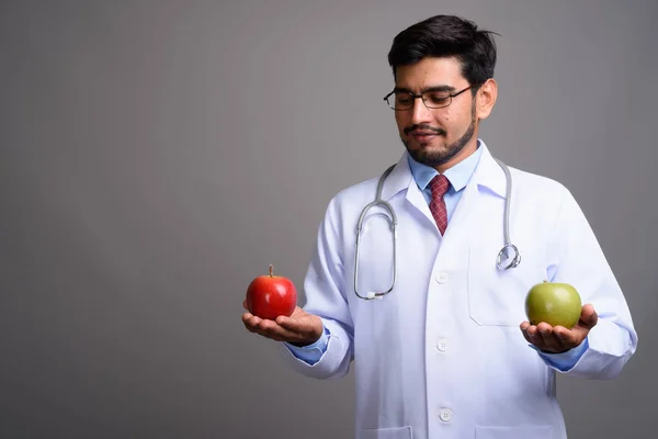 Young handsome bearded Persian man doctor against gray backgroun — Stock Photo, Image